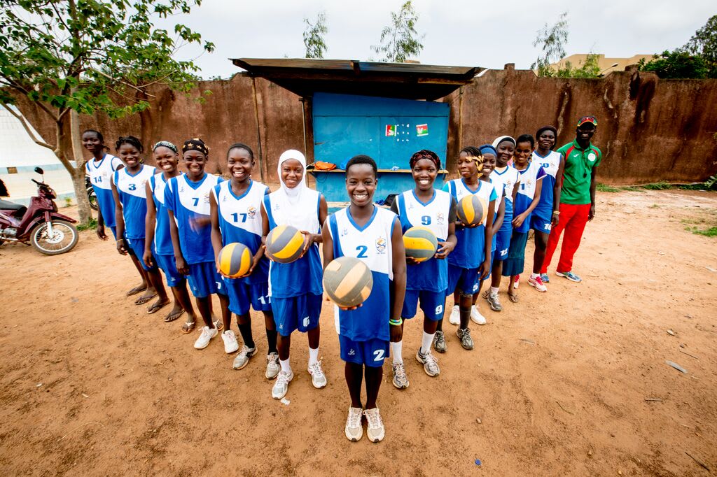 Zangre and her volleyball team stands in a v-formation holding volleyballs